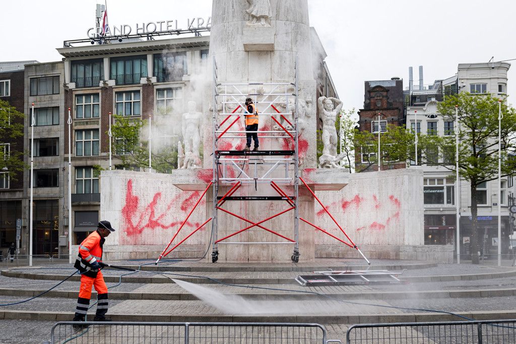 schoonmakers halen rode verf van het nationaal monument op de dam